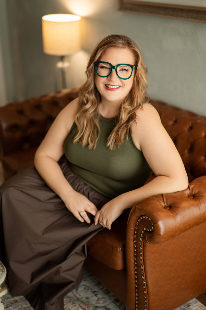 Kristine Depies, founder of KAYDEE Management Solutions, smiling while seated on a brown leather couch in a relaxed professional portrait. Part of the Power of Her campaign by Kara Reese Photography.
