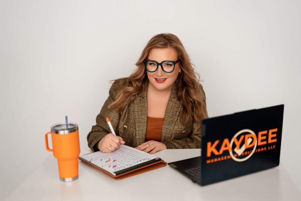 Professional headshot of Kristine Depies, founder of KAYDEE Management Solutions, seated at a desk with a laptop, notebook, and orange tumbler. Photo by Kara Reese Photography in Waukesha, WI